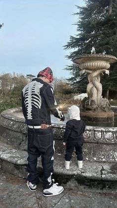 a man standing next to a little boy near a fountain with a skeleton on it