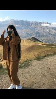 a woman standing on top of a hill taking a photo with her cell phone in the mountains