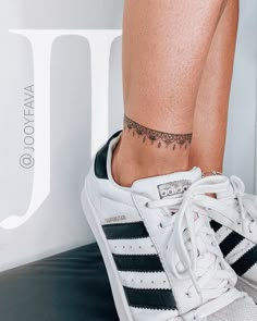 a woman's foot with a small tattoo on her left ankle and white adidas sneakers