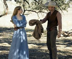 a man and woman dressed in western clothing standing next to each other under a tree