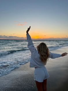 a woman standing on top of a sandy beach next to the ocean at sun set