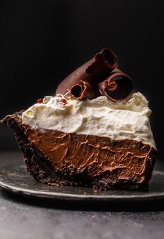 a piece of chocolate pie with whipped cream and chocolate pieces on top, sitting on a plate