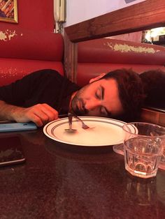 a man sleeping on a table with a plate and fork in front of his face