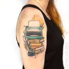 a woman with a book and typewriter tattoo on her left arm, next to a stack of books