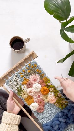 a woman sitting on the floor working on a piece of art with yarn and knitting needles