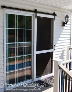 an open sliding glass door on the side of a white house with black shutters