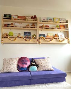 a purple couch with pillows on it in front of two wooden shelves filled with books