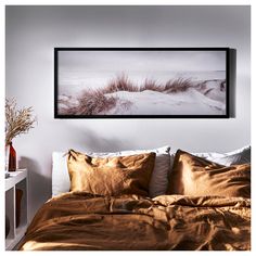 a bed with brown sheets and pillows in a room next to a painting on the wall