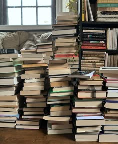 a large stack of books sitting on top of a wooden floor next to a window