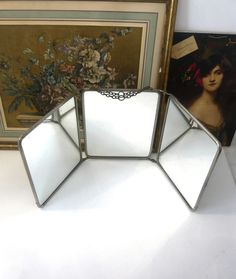 three mirrors sitting on top of a table next to pictures and framed art pieces in the background