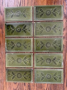 six green tiles with flowers and leaves are arranged on a wooden surface, one is missing the