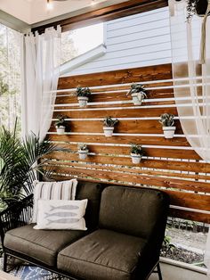 a couch sitting in front of a window next to a wooden wall with potted plants on it