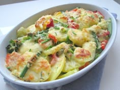 a casserole dish with vegetables in it on a white tablecloth next to a blue napkin