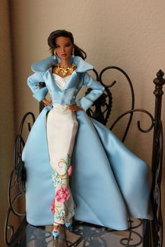 a barbie doll sitting on top of a bed with blue and white dress, gold necklace and shoes