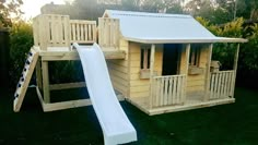 a wooden play house with a slide and climbing frame in the back yard at sunset