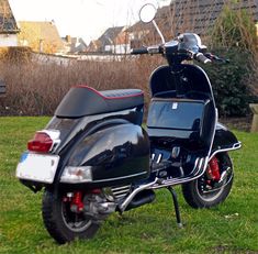 a black scooter parked on top of a green grass covered field next to a building