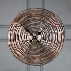 a clock made out of copper colored metal tubes on a white wall with grey background