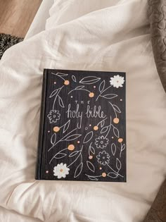 a book that is laying on top of a bed with white sheets and flowers around it