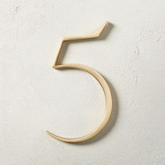 the number five is made from wood and sits on a white wall in front of a stucco background