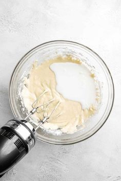 an electric hand mixer mixing batter in a glass bowl on a white surface with a black beater