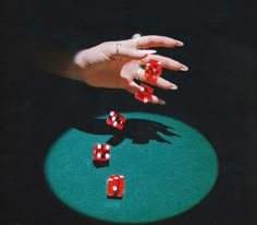 a woman's hand reaching for red dices on a green surface with shadows