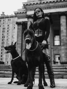 a woman standing next to two dogs in front of a building