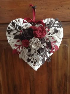 a heart shaped decoration hanging on a door with red, white and black flowers in it