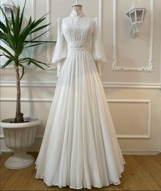 a white wedding dress on display next to a potted plant