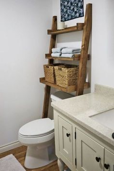 a white toilet sitting next to a bathroom sink under a wooden shelf filled with towels