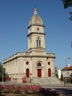 an old building with a clock tower on it's side and flowers in the foreground