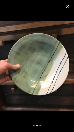 a hand holding a green and white plate on top of a wooden table next to a drawer