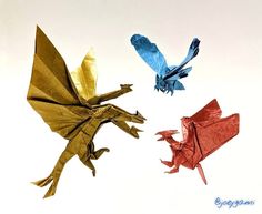 three different colored origami birds flying in the sky