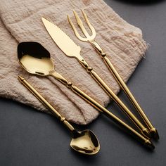 four gold colored utensils are on a napkin next to a fork, knife and spoon