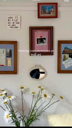 a vase filled with white daisies sitting next to pictures on the wall above it