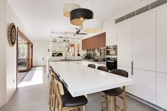 a kitchen with white counter tops and wooden stools next to an open floor plan