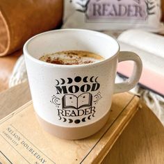 a cup of coffee sitting on top of a wooden table next to a book and pillow