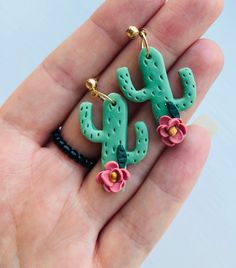 a person is holding two earrings in their hand, one has a cactus and the other has flowers