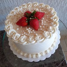 a cake with white frosting and strawberries on top is sitting on a glass table