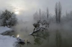 the sun shines through the foggy sky over a river with snow on it