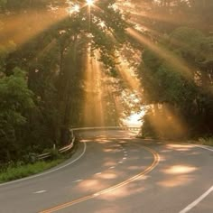 the sun shines brightly through the trees on an empty road