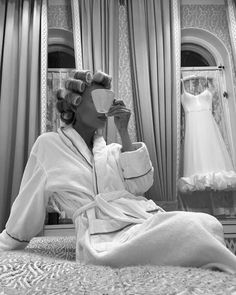 a woman sitting on top of a bed drinking from a cup in front of a mirror