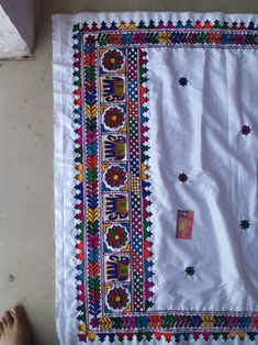 a person standing next to a white table cloth with colorful designs and beads on it