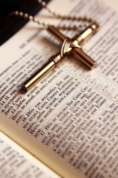 an open book with a cross on top of it and a chain hanging from the front