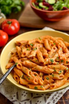 a yellow bowl filled with pasta on top of a table next to tomatoes and lettuce