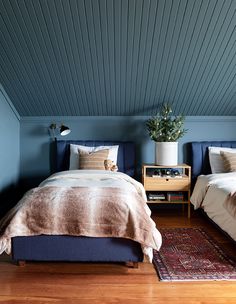 two beds in a room with blue walls and wooden floors, one has a teddy bear on the bed