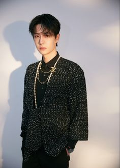 a young man wearing a black shirt and pearls on his neck standing in front of a white wall