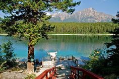 a red bridge leading to a lake with mountains in the background and trees on either side