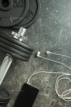 an electronic device connected to a barbell on the ground next to a pair of headphones