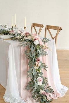 the table is decorated with pink flowers and greenery, along with candles on either side