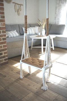 a living room with a couch, chair and rope hanging from the ceiling in front of a brick wall